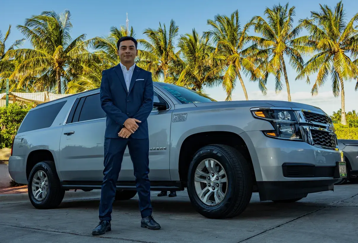 Prestige chauffeur in a white uniform next to a white Chevrolet Suburban at a resort lobby
